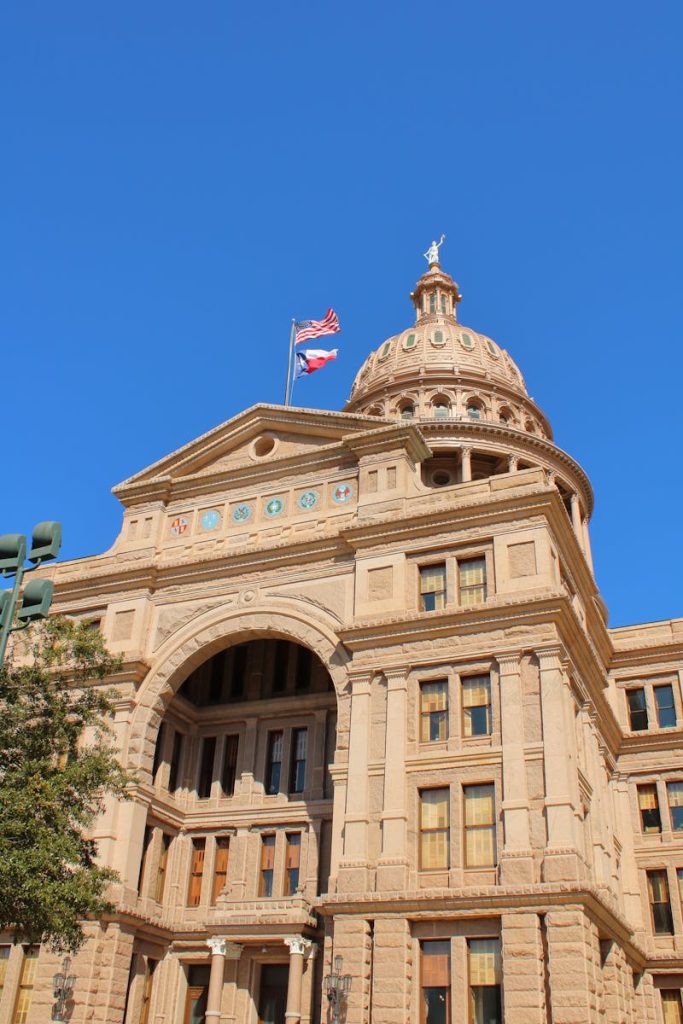 A vertical shot of the Texas State Capitol building exterior under a clear blue sky.