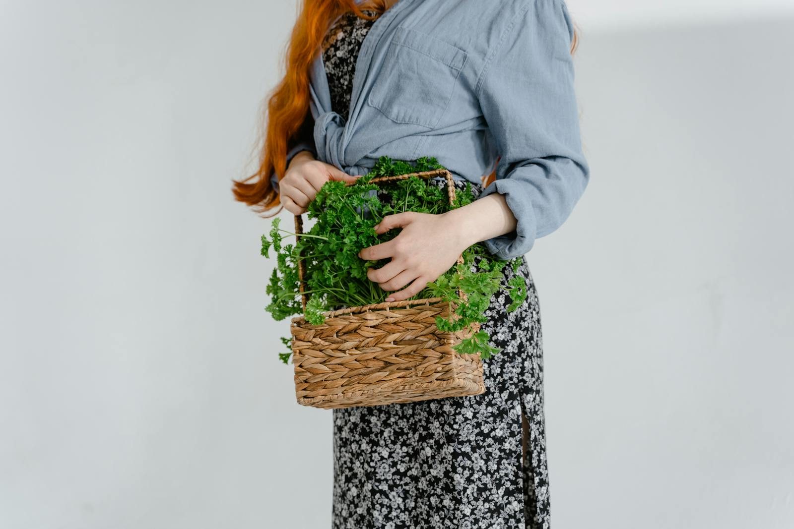 Carmela Clouth A woman holds a woven basket filled with fresh parsley, symbolizing eco-friendly living and natural lifestyle.