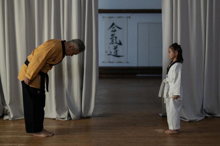 Karate instructor bowing to a young girl in martial arts uniform, showing respect.