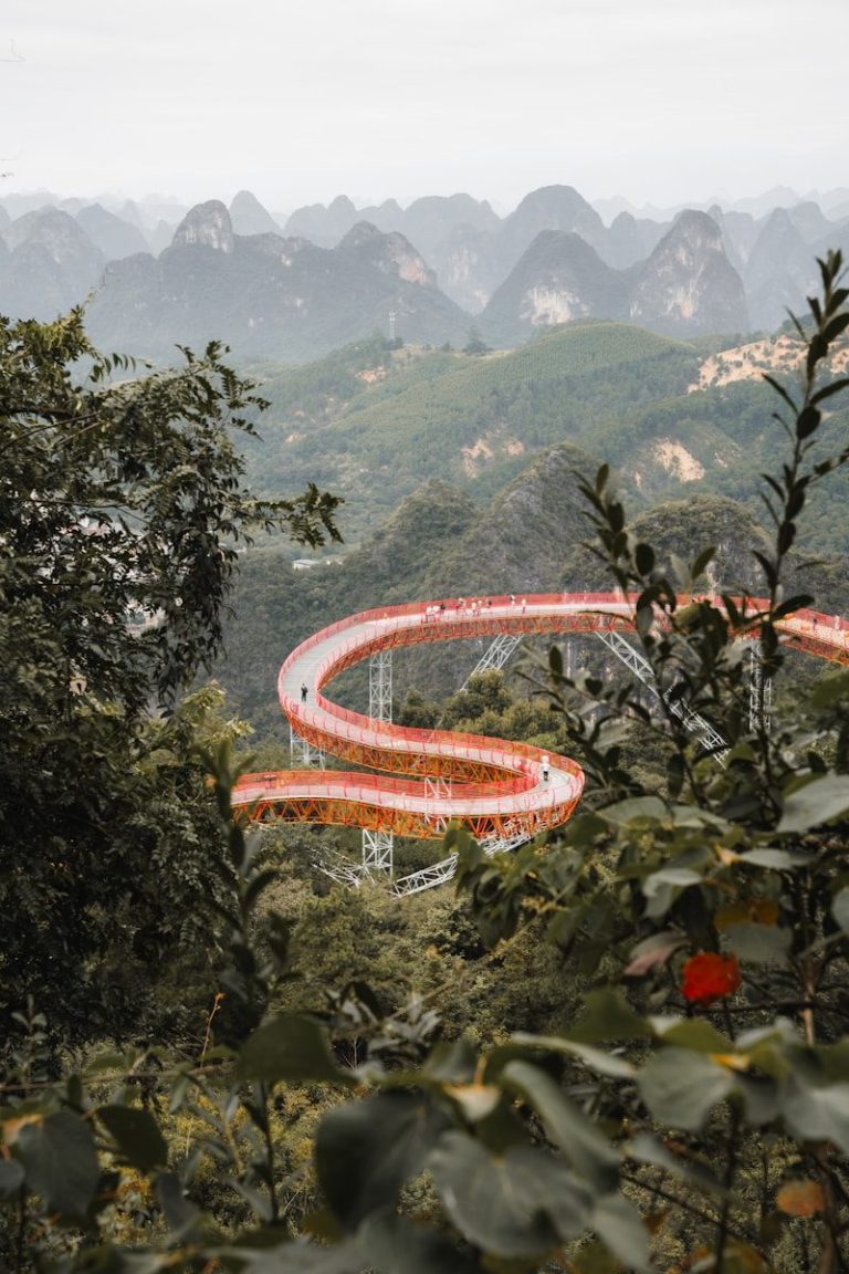 Curving bridge winds through lush green mountains under hazy sky.